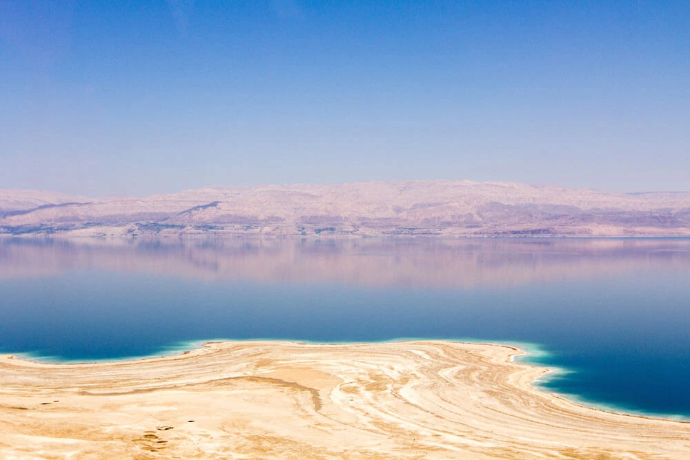 The front of Dead Sea in Jordan surrounded by sandy beach and blue sky in the horizon 