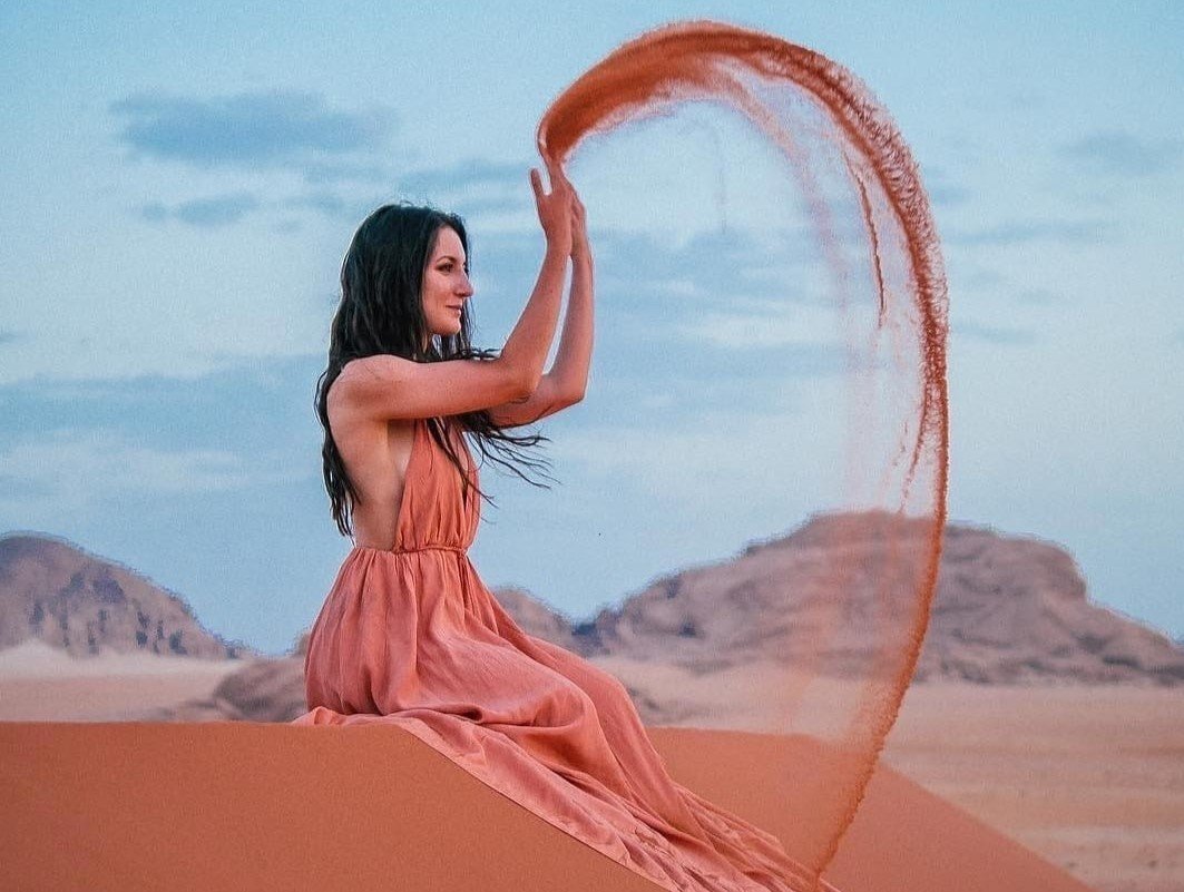 A girl sits on a sandy hill in the Wadi Rum desert in Jordan.
